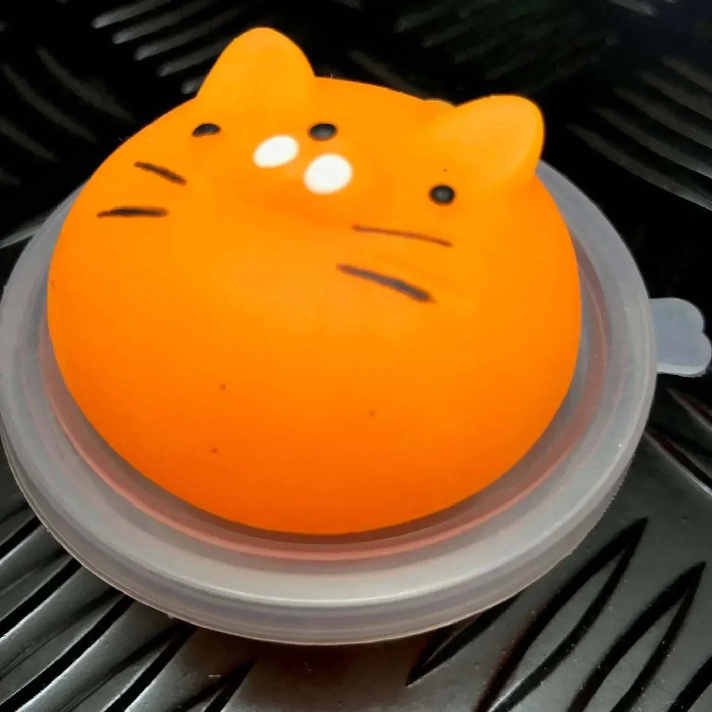 Orange jelly mochi squishy animal toy shaped like a cat face on a black textured surface