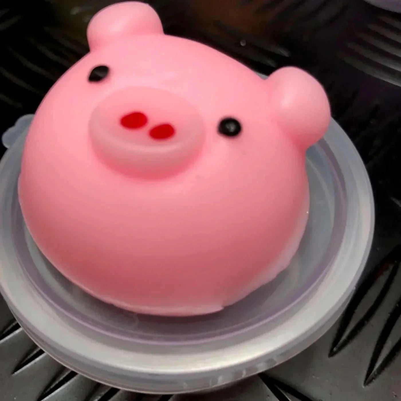 Pink Jelly Mochi Squishy Animal shaped like a pig with black eyes and red nostrils on a round clear base