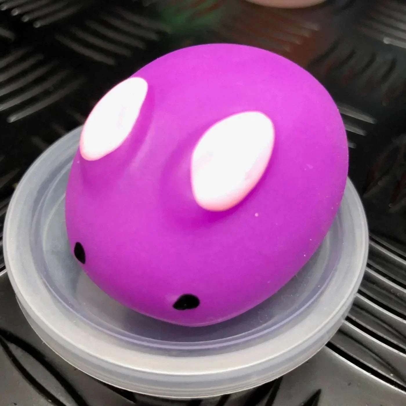 Purple Jelly Mochi Squishy Animal with white eyes on a clear plastic lid